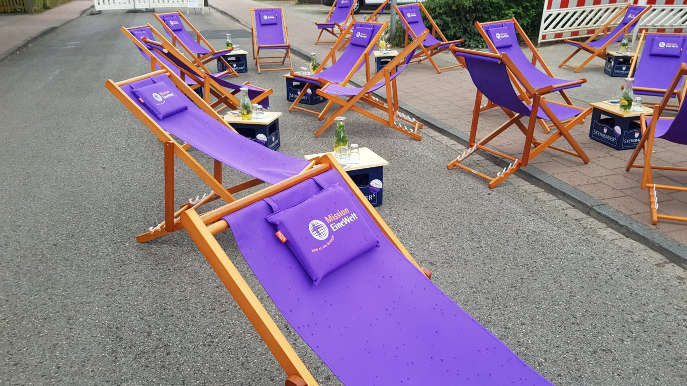 Mehrere lila Liegestühle mit Holzbasis stehen auf einem Bürgersteig.
