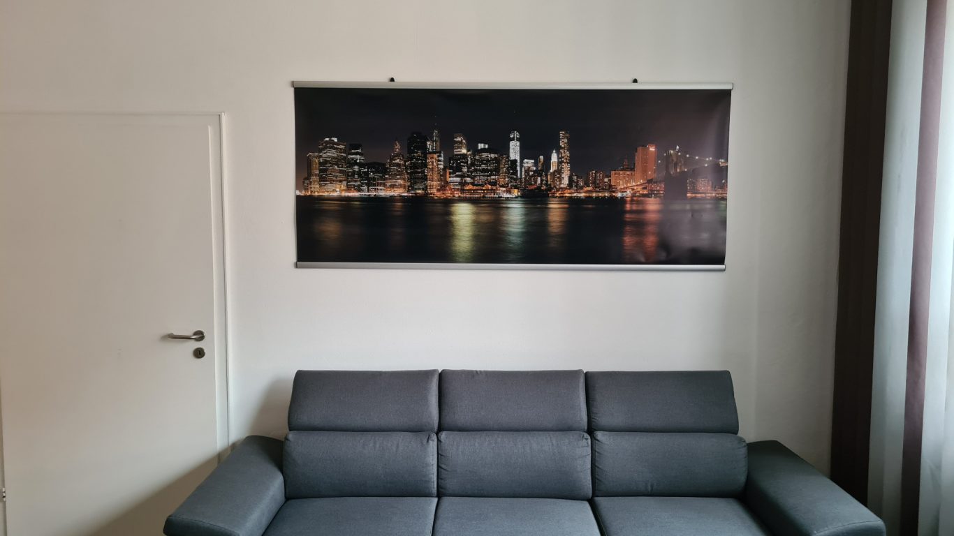 Stadtansicht bei Nacht mit beleuchteter Skyline und einem grauen Sofa im Vordergrund.