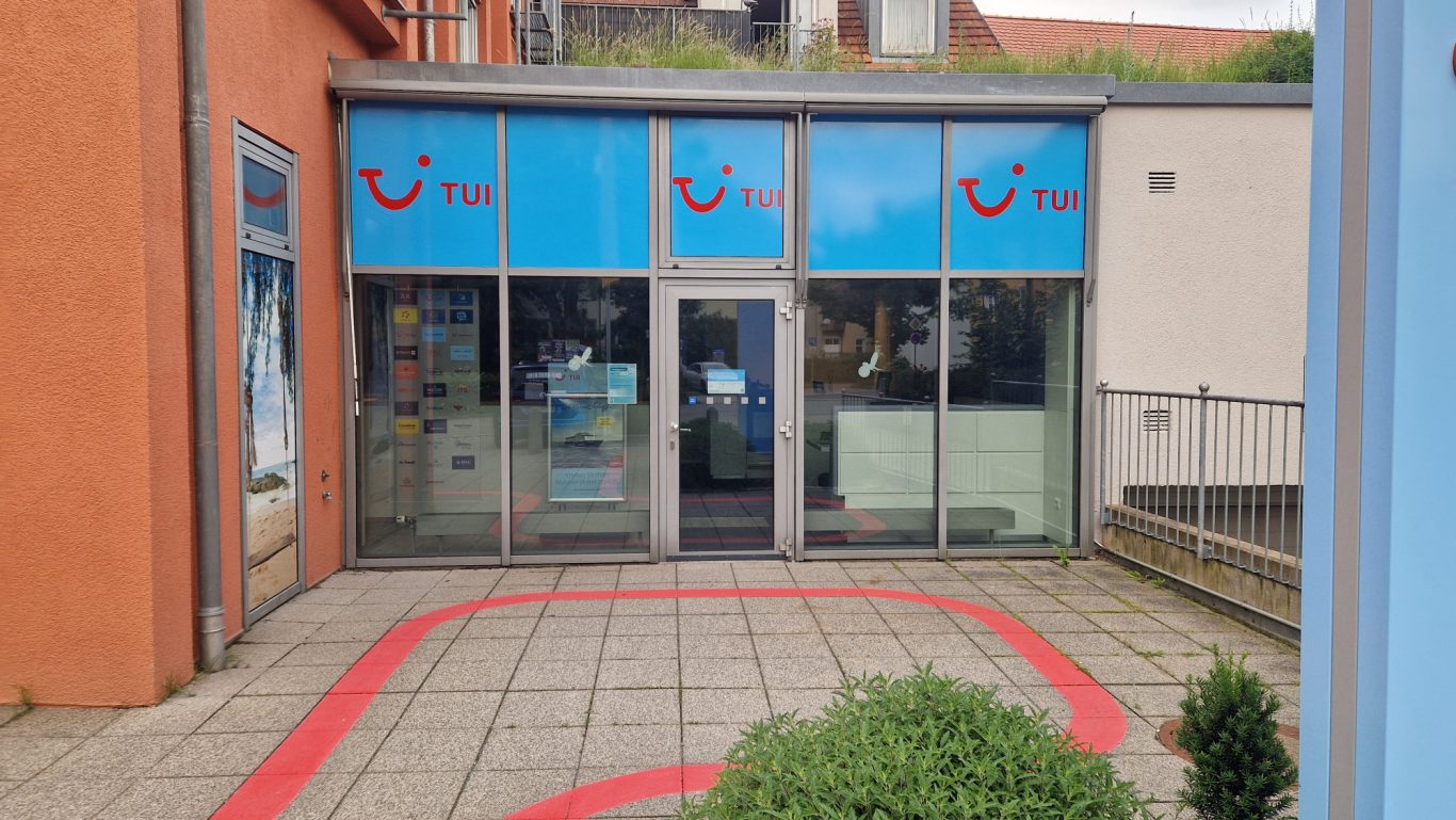 Fassade eines Büros mit blauer Beschilderung und roten Akzenten.