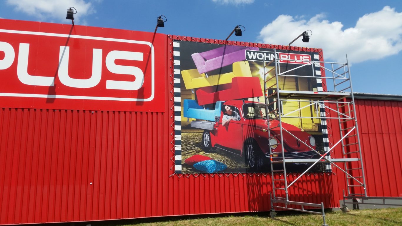 Rotes Gebäude mit Plakat einer roten Fahrzeugillustration und Baugerüst.